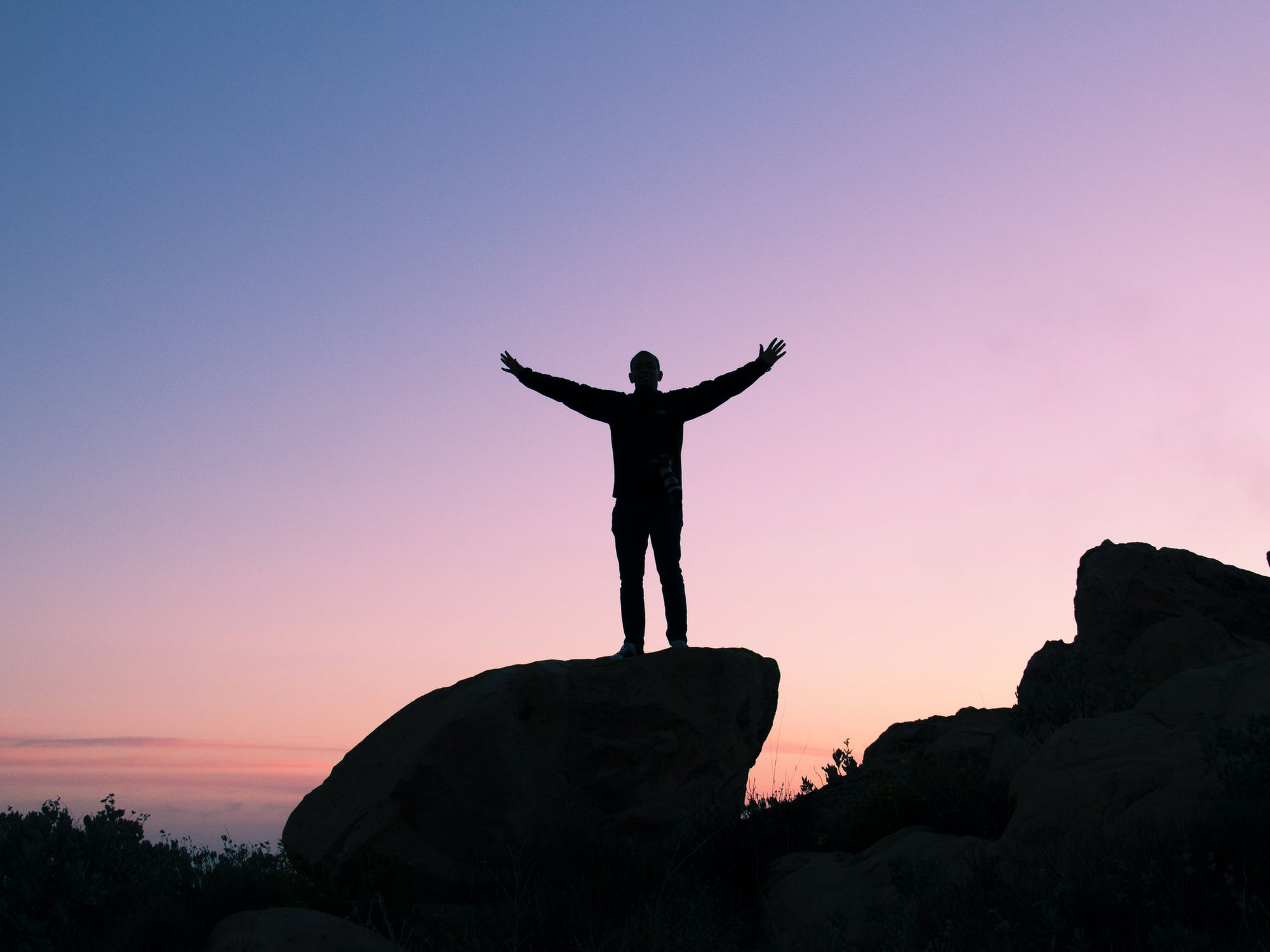 A silhouette of a person standing on a rock with their arms outstretched.