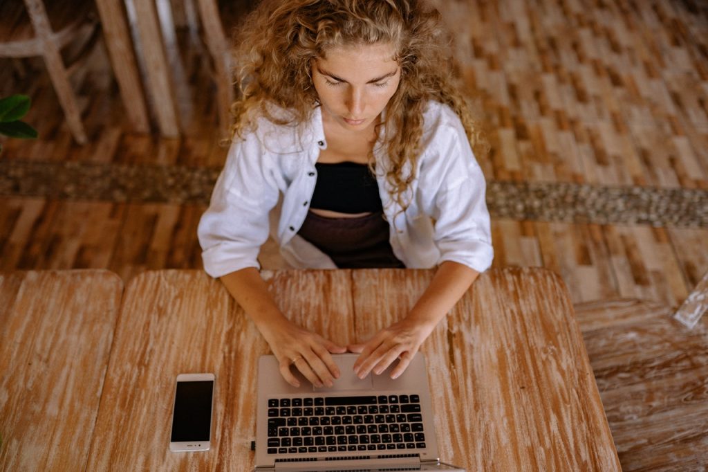 A woman sits at a wooden desk while using a desktop computer.