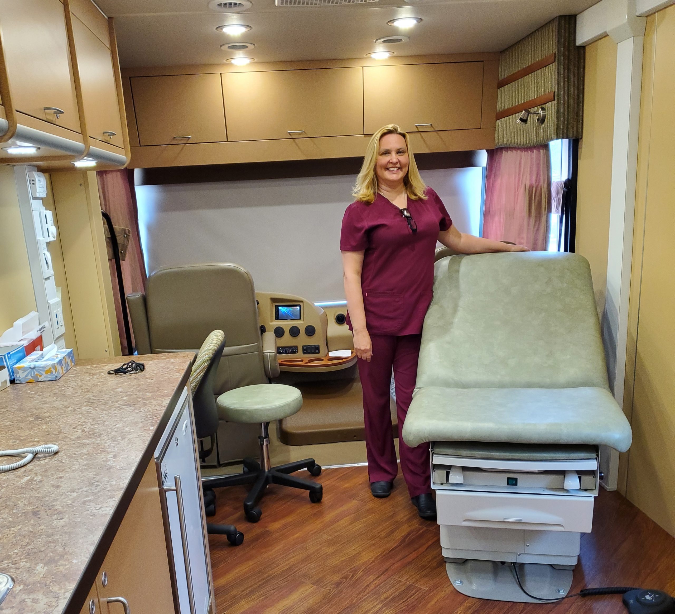 A woman in scrubs stands next to a medical bed in our mobile unit.