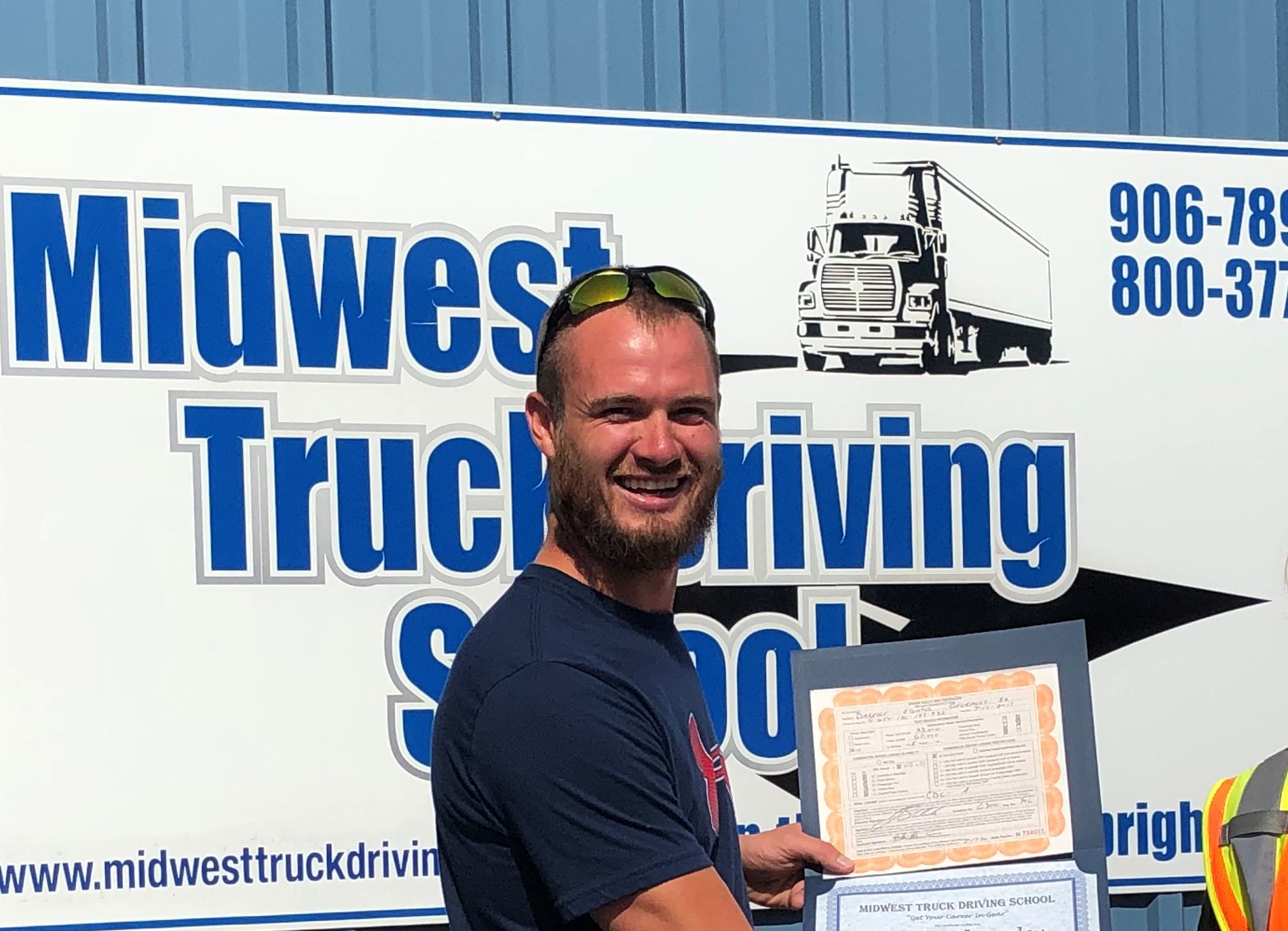 Darelle poses in front of a Midwest Truck Driving Sign with his certificate.