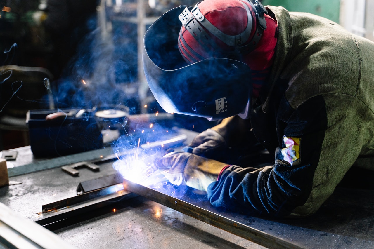 A person in welding gear uses a welding machine to weld metal.