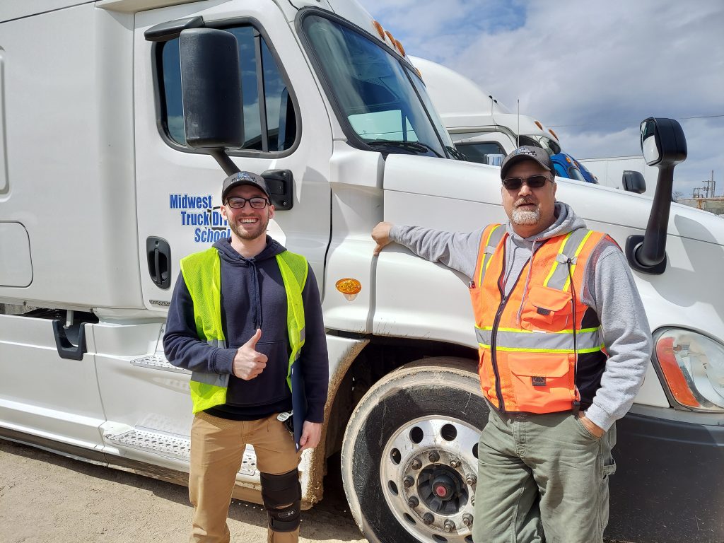 Jacob and his trainer stand in front of a Midwest Truck Driving School truck.