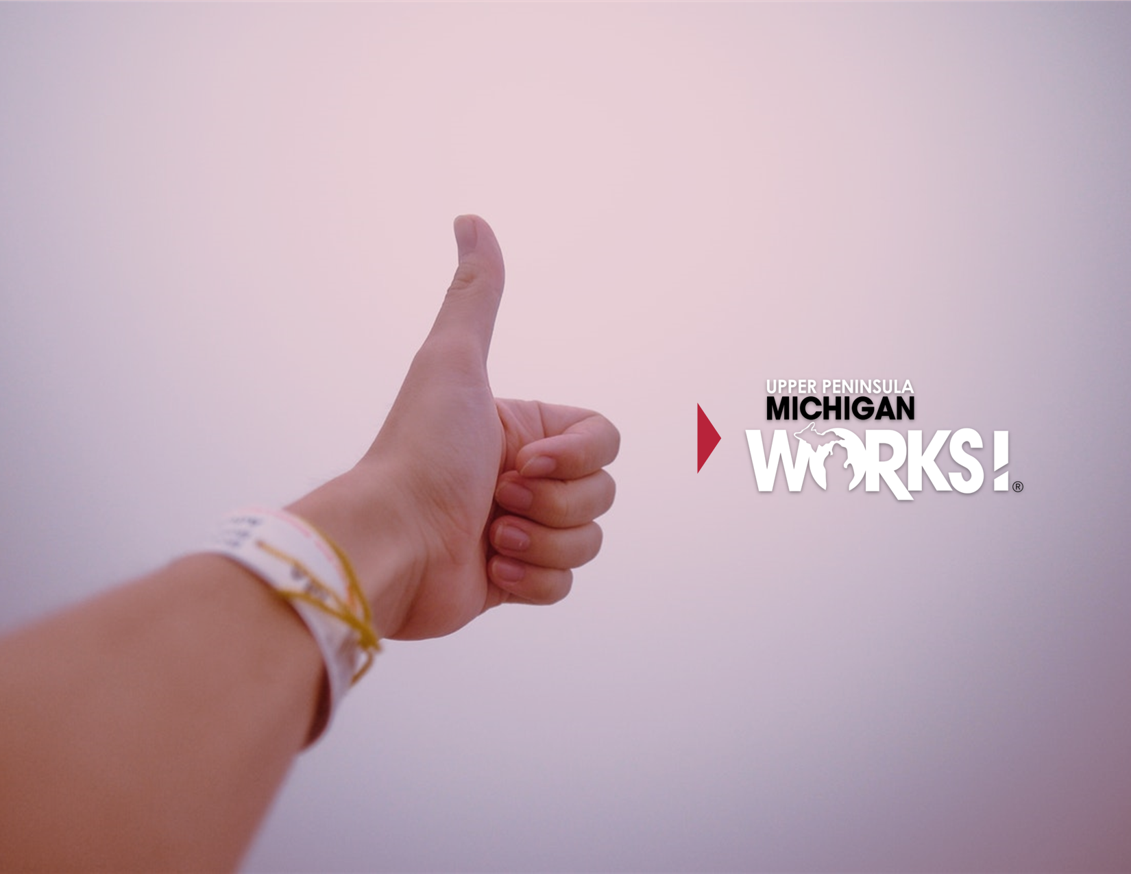 A person gives a thumbs up with the UP Michigan Works logo overlayed.