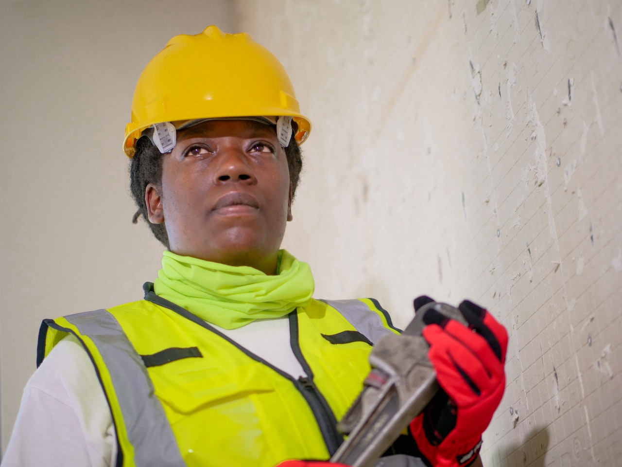 A woman in a hard hat and vest holds a tool.