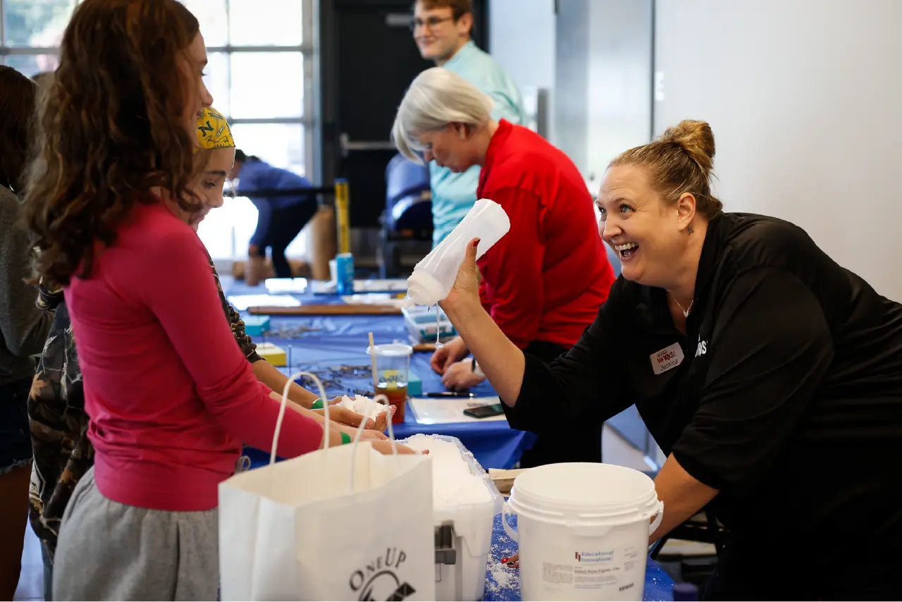 Mind Trekkers Promo Picture. Michigan Works employee leans over demonstration table to show a student how to spray water