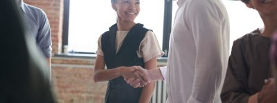 A man and a woman shaking hands in a room with brick walls and large windows behind them.